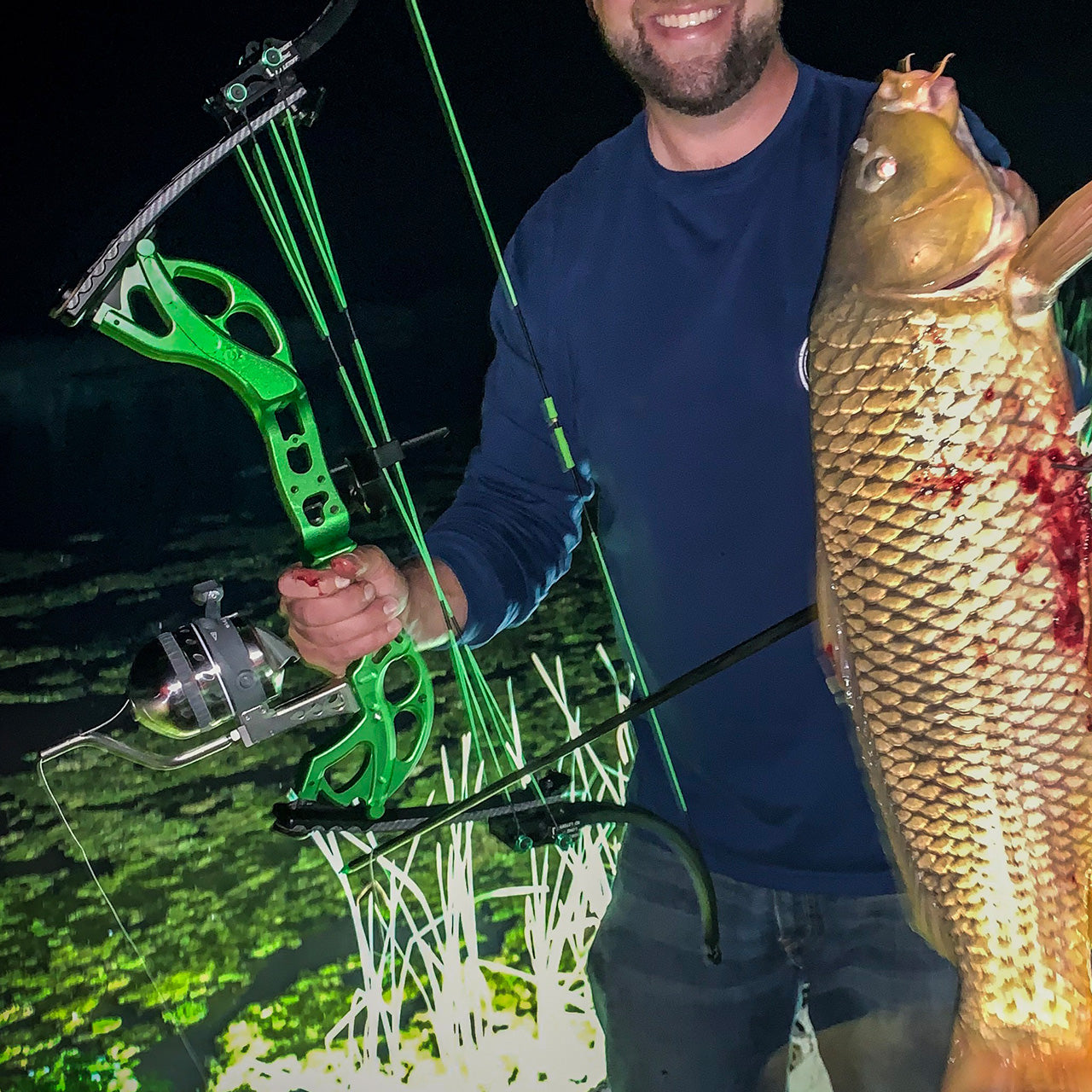 Bright green compound bow with illuminated reels held by angler at night.