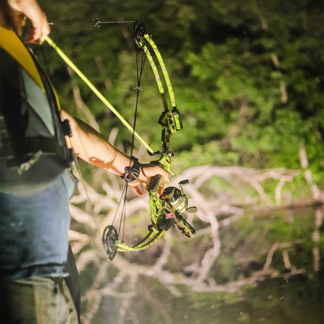 Bright green and black compound bow with illuminated sight in nighttime forest setting.