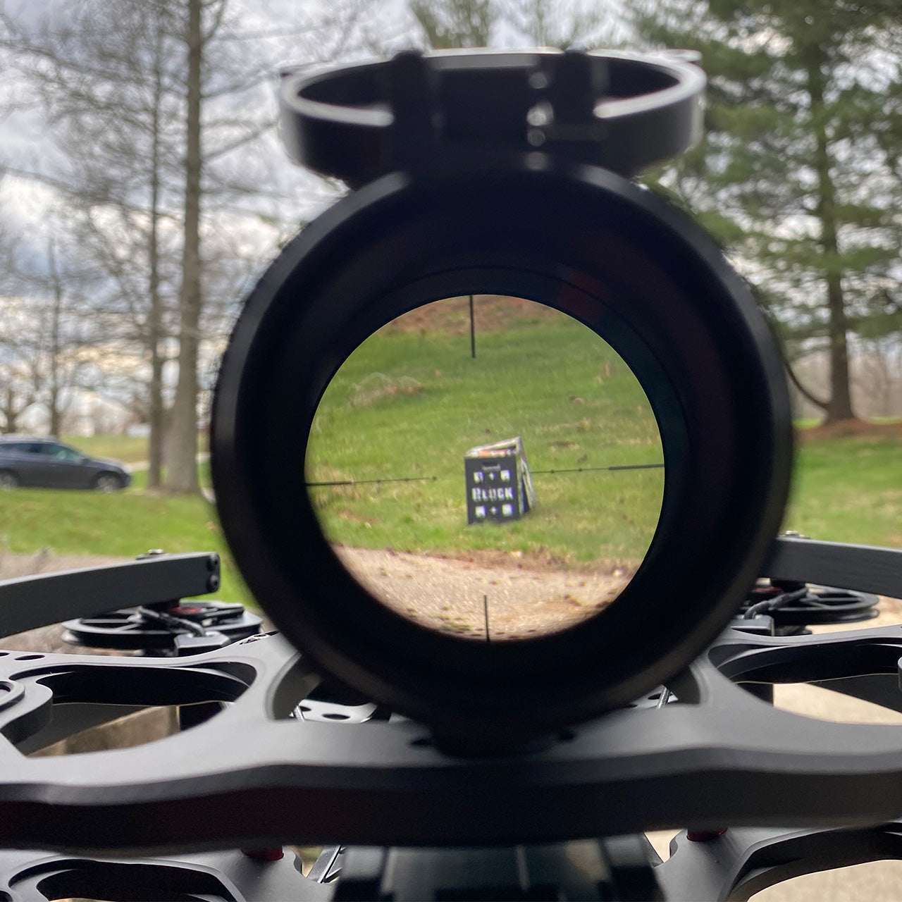High-powered rifle scope looking at a black block target outdoors on a grassy field.