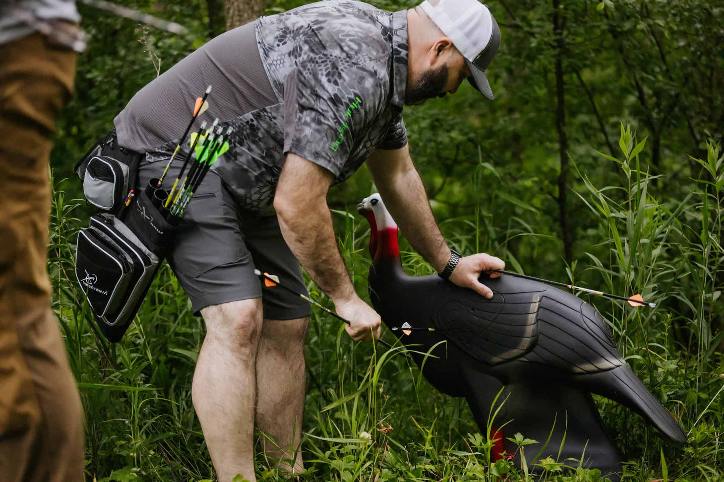 1. Man practicing bowhunting with FeraDyne archery gear in lush forest.