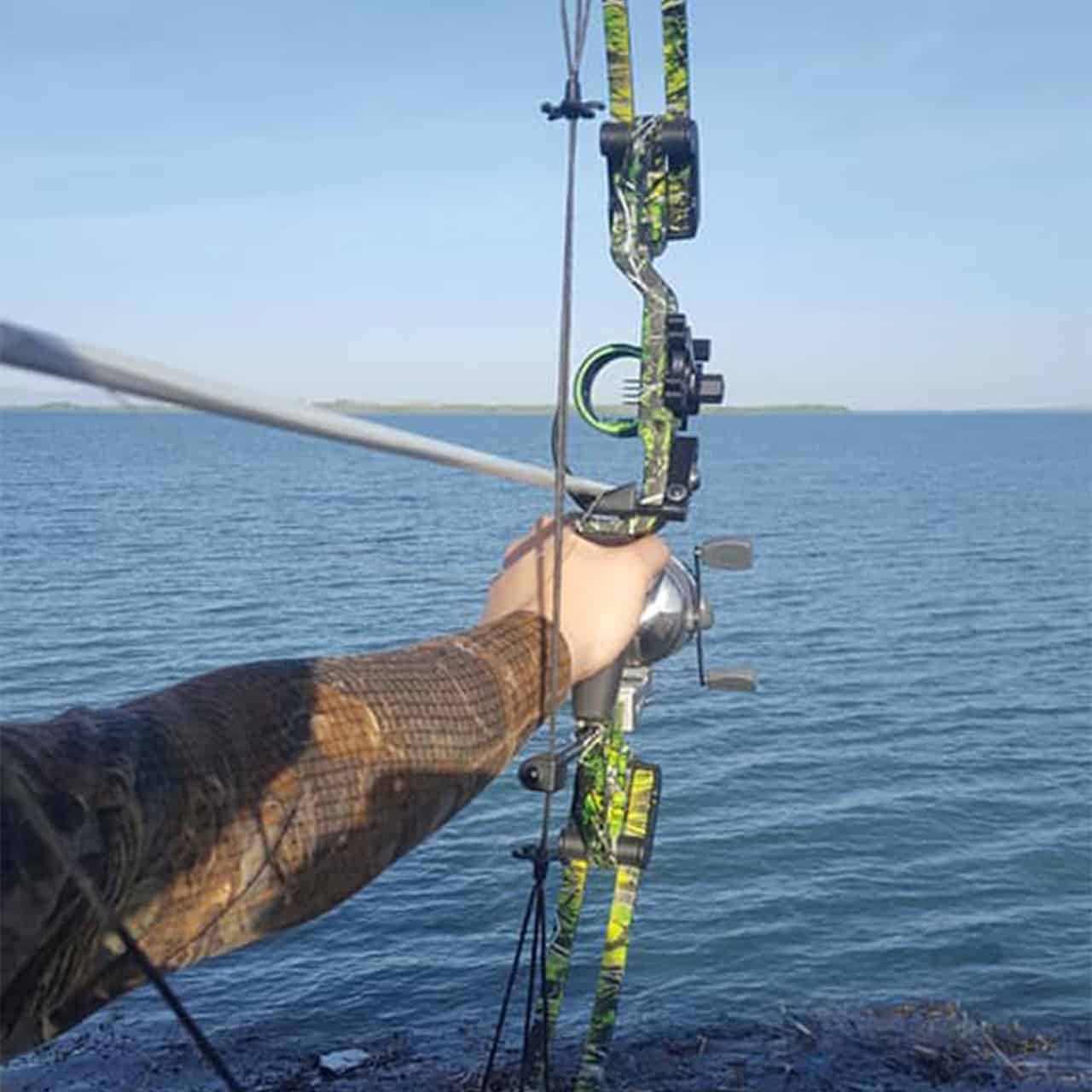 Bright green camo compound bow with sight and stabilizer, held over water for outdoor bowhunting.