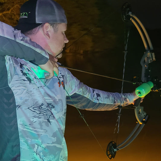 1. Man practicing archery at night with a bow and arrow, illuminated by headlamp.