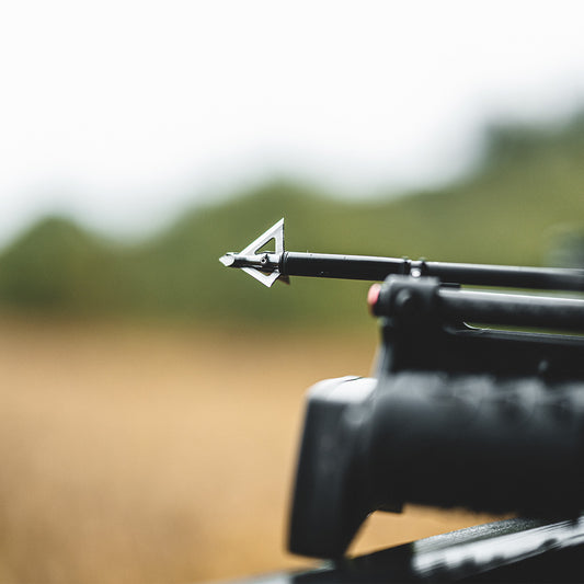 Precision crossbow bolt on a black bow, outdoor hunting setup with blurred background.