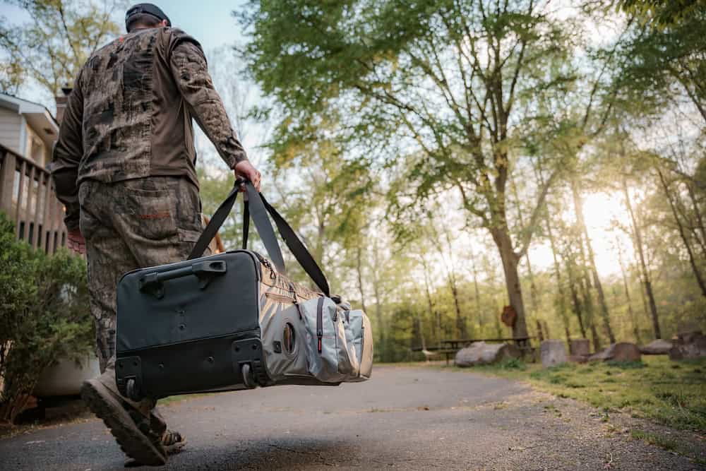 Duffle bag being carried outdoors during daytime with trees and sunlight in background.