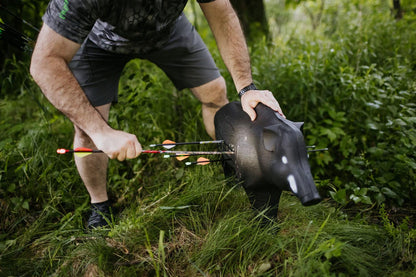 Compact black rubber pig decoy with arrows lodged in its side for bowhunting practice or tactical training.