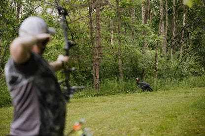 1. Person aiming a bow at a turkey decoy in wooded outdoor setting.
