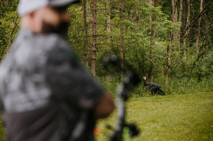 Aiming at a turkey decoy in a wooded outdoor setting for bowhunting.