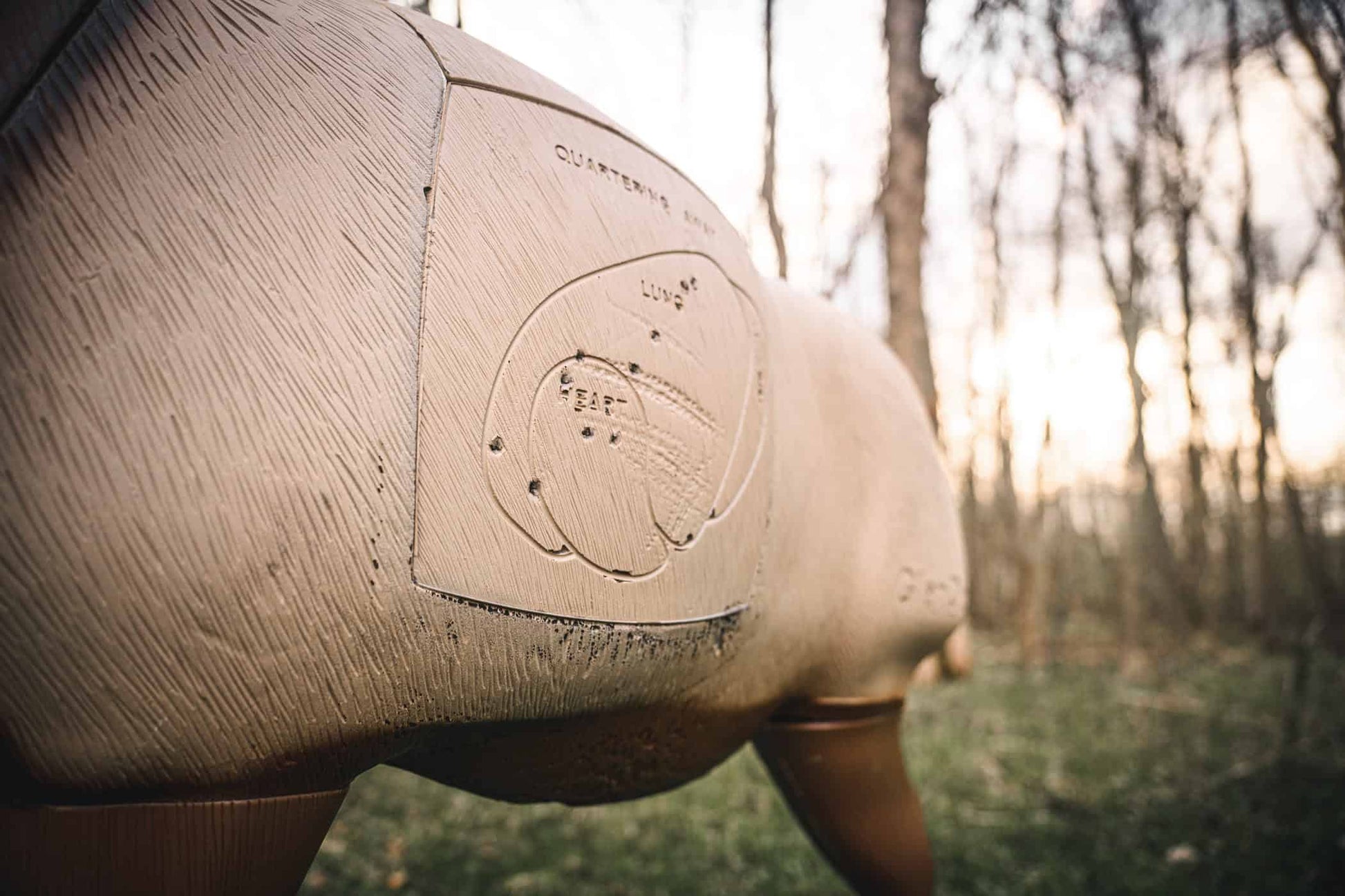 Smooth wooden archery target with detailed shot placement markings in a wooded outdoor setting at sunset.
