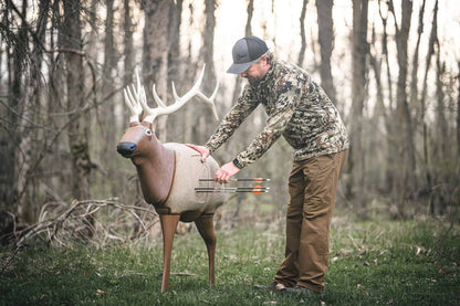 Real or simulated deer target in a wooded outdoor setting for archery practice.