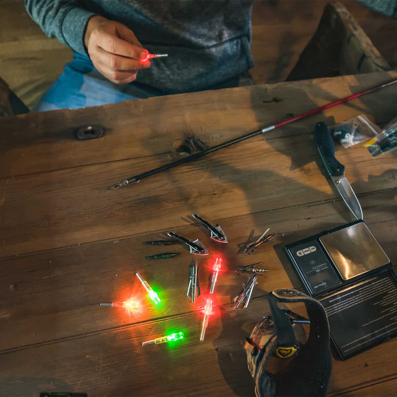 Small fishing hooks with LED lights on a wooden table for night fishing or lure setup.