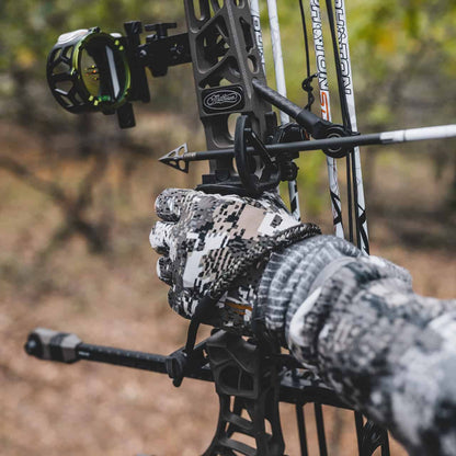Precision archery setup in outdoor woodland setting with camo gloves and high-tech bow equipment.