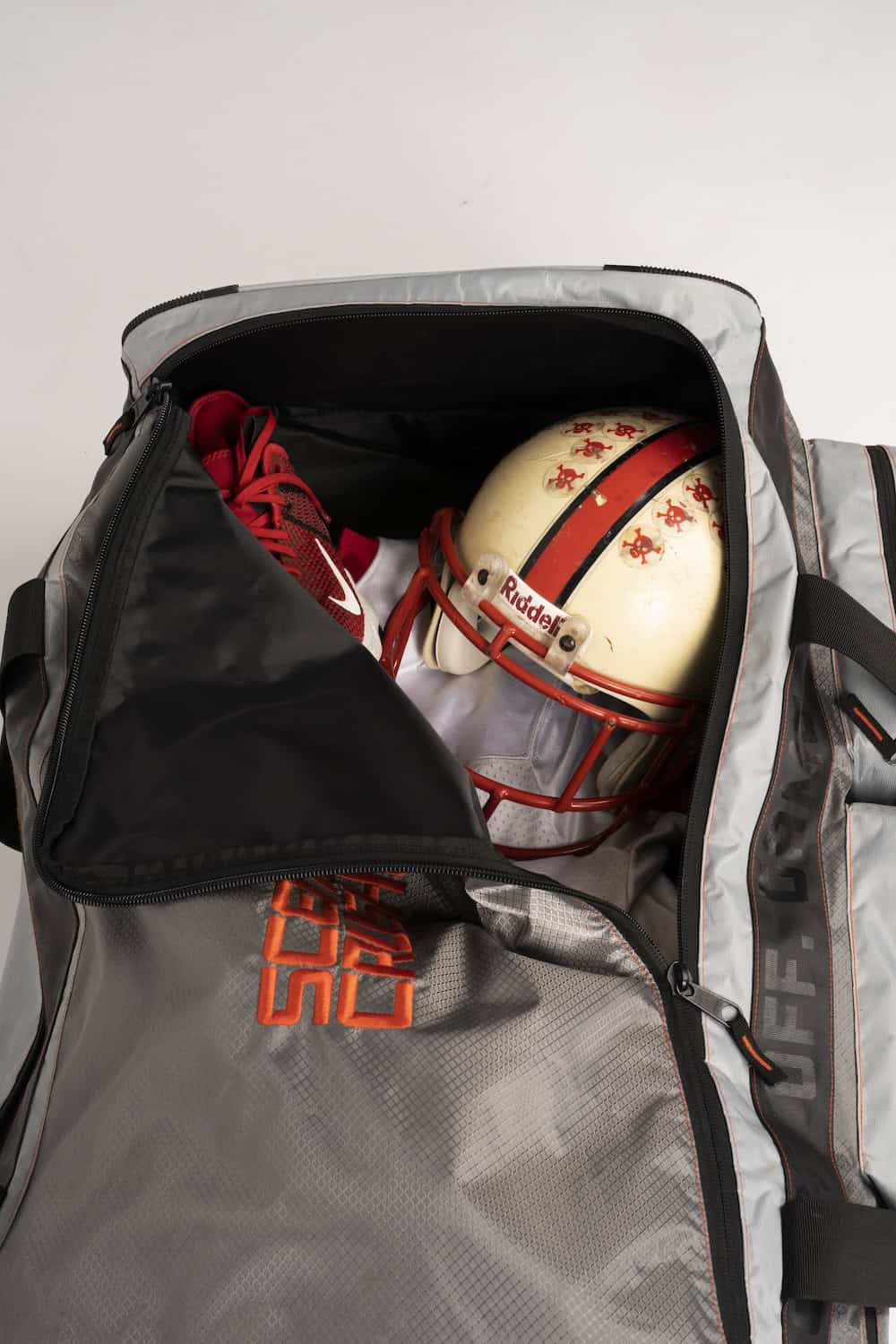 Athletic football helmet inside a sports duffel bag with red sneakers for training or game.