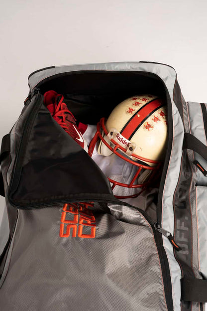 Athletic football helmet inside a sports duffel bag with red sneakers for training or game.