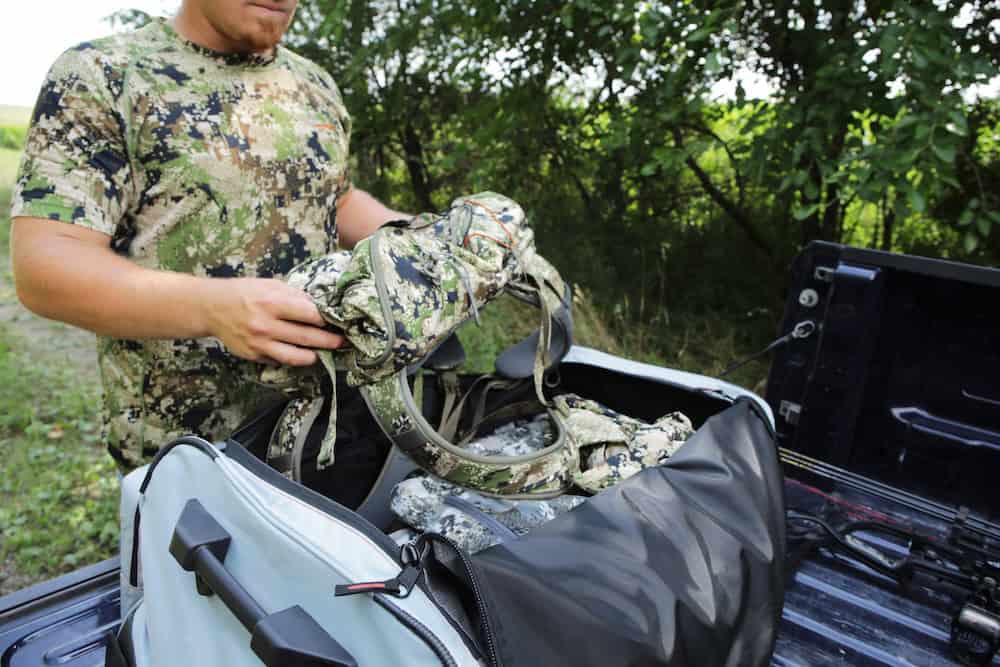Camouflage hunting gear being packed in a truck bed in outdoor woodland setting.