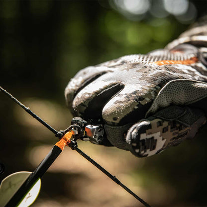 Camouflage tactical glove on a hunter's hand holding a bowstring in outdoor setting.