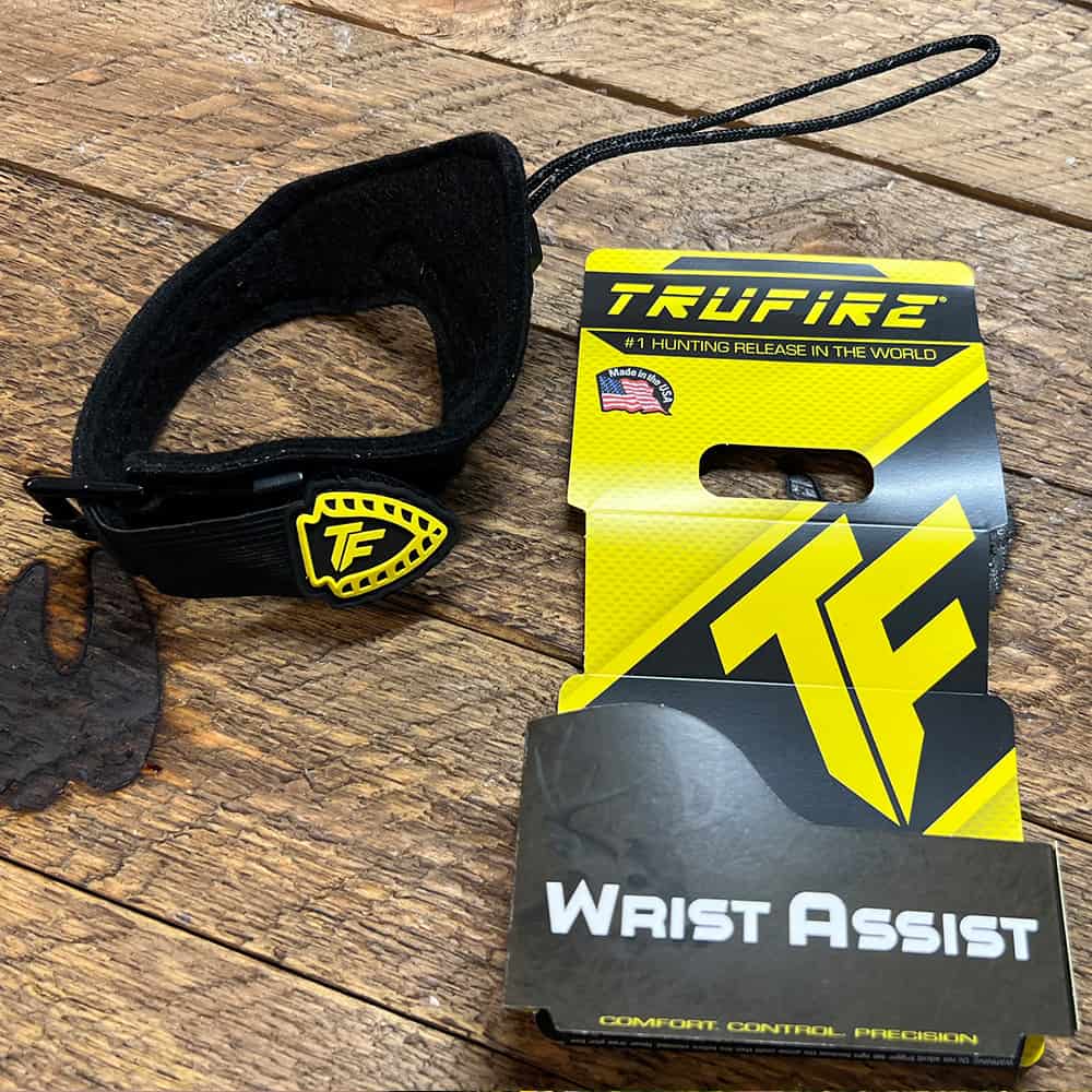 Adjustable archery wrist release aid with supportive strap on rustic wooden surface.