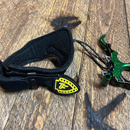 High-performance bow release with adjustable strap on a rustic wooden surface.