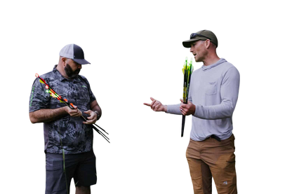 Bright outdoor scene of two men preparing for bowhunting with a deer target and arrows in a forest setting.
