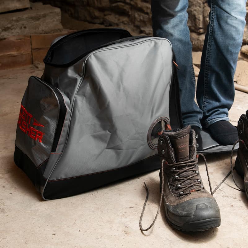 Heavy-duty black and gray hunting gear bag with orange accents and a side pocket, placed on a rustic wooden floor.