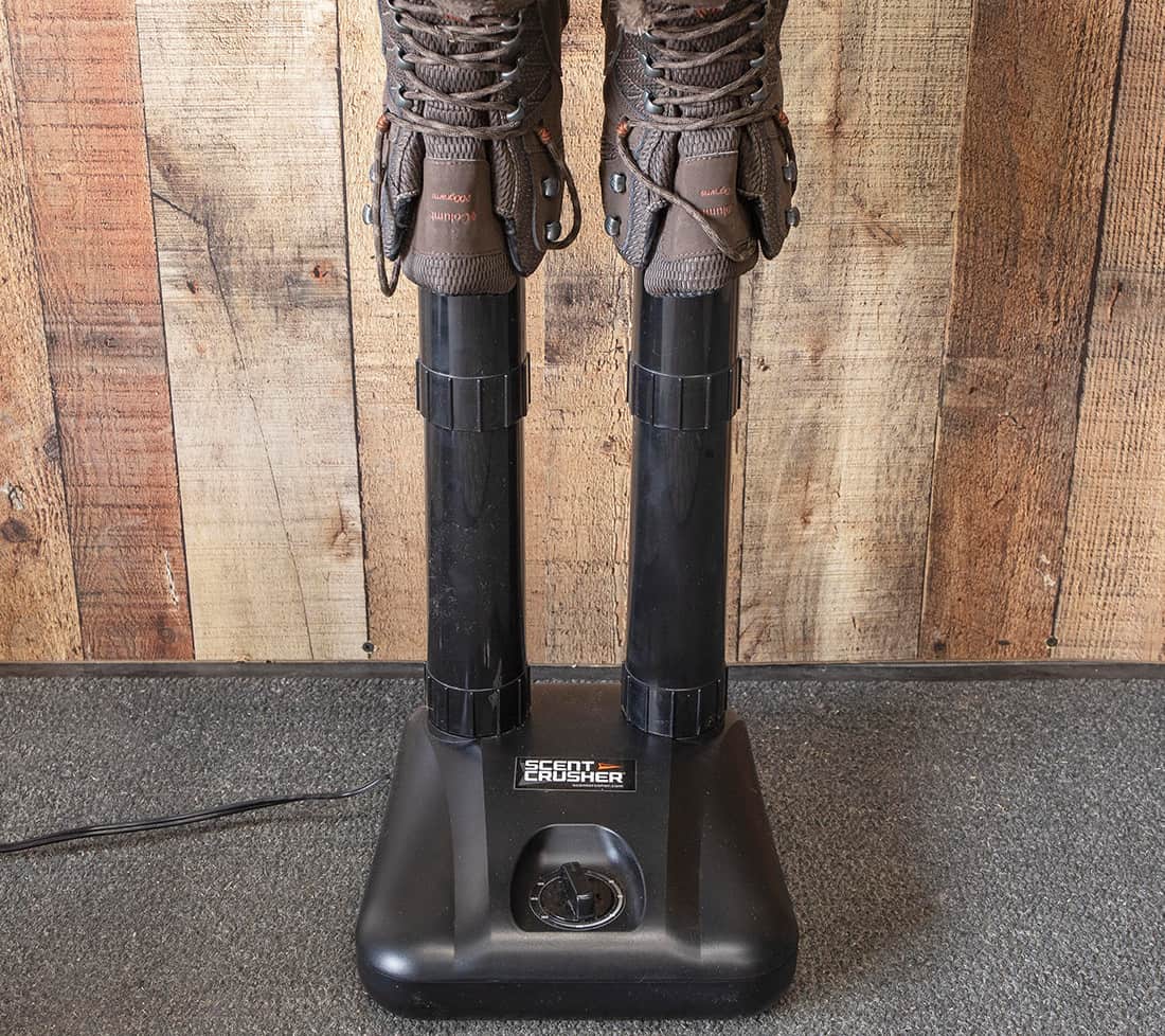 Two pairs of hiking boots mounted on a scent elimination machine on a textured gray floor.