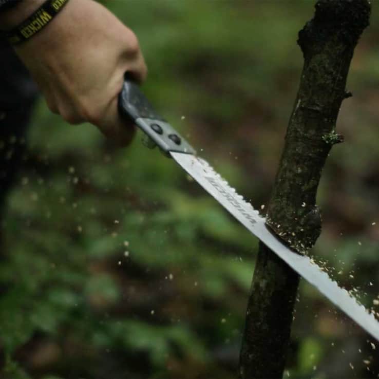 Sharp survival knife cutting through a tree branch in the forest for outdoor enthusiasts.