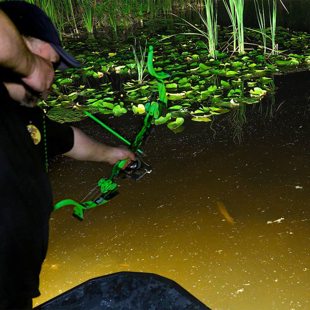 Bright green compound bow with stabilizer aimed at water surrounded by lily pads and reeds.
