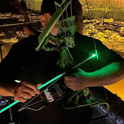 Night archery hunting with illuminated bow and arrow in a wooded area.